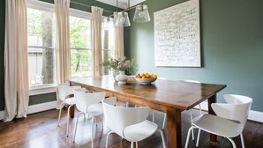 A dining area with a wooden table, white chairs, and a bowl of fruit.