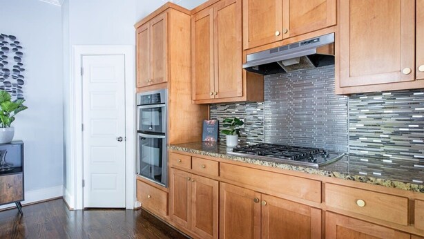 A kitchen with wooden cabinets, a stainless steel range hood, and a tiled backsplash.