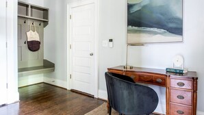 A room with a wooden desk, a chair, a bookshelf, and a painting on the wall.