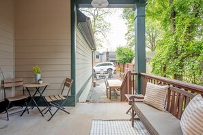 A covered patio with a wooden bench, a small table, and folding chairs.