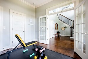 Een sportschool in huis met trainingsapparatuur, een trap en uitzicht op buiten.