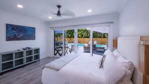 A bedroom with a large bed, a TV, and a view of a pool and outdoor seating area. - Sun-Kissed Bungalow w/ Pool + Spa (Naples)