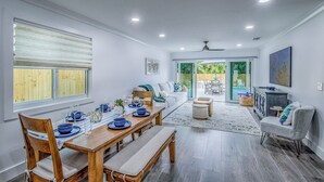 A dining area with a wooden table set for four, a sofa, and a view of a backyard with a pool. - Sun-Kissed Bungalow w/ Pool + Spa (Naples)