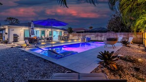 A backyard with a swimming pool, patio furniture, and a wooden fence. - Sun-Kissed Bungalow w/ Pool + Spa (Naples)