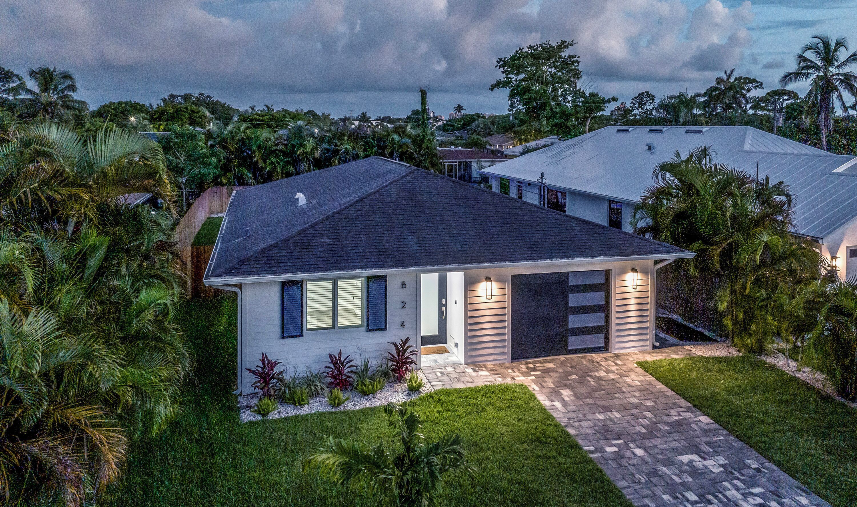A modern two-story house with a dark roof, a front entrance with a light fixture, and a well-maintained lawn.