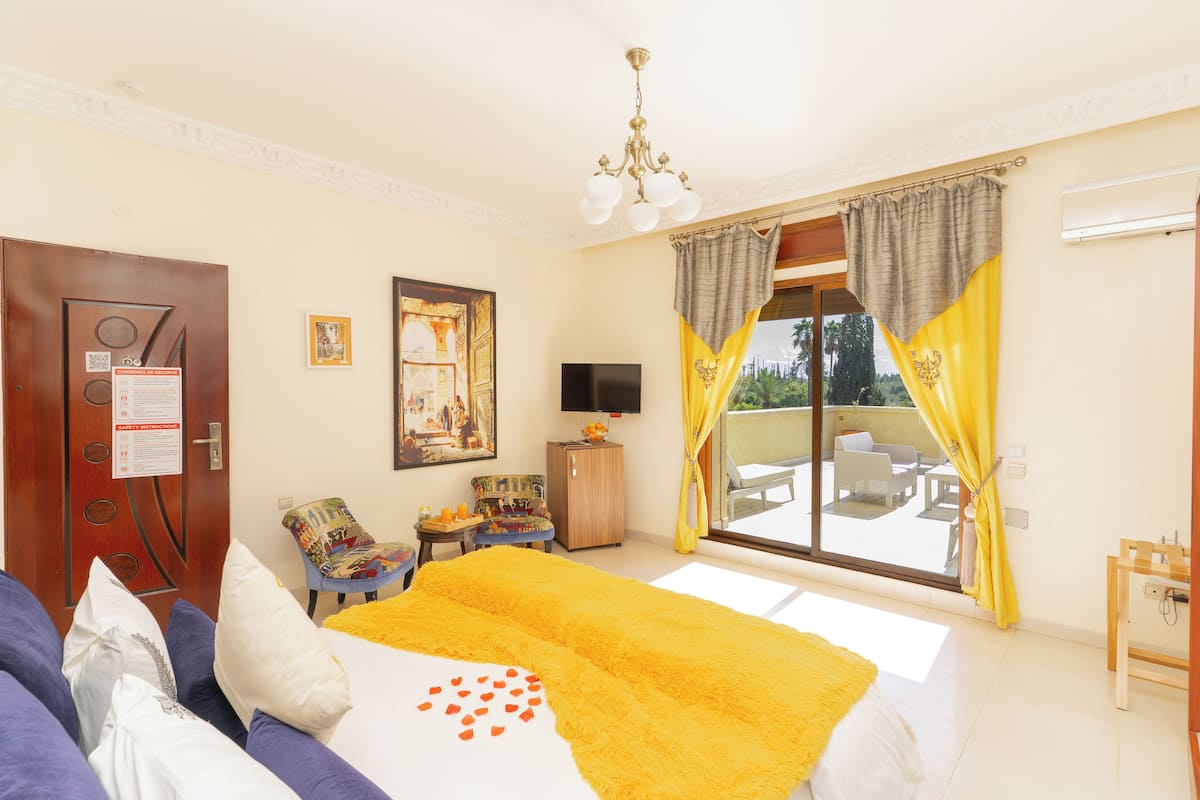 A hotel room with a bed, a television, a chair, a small table, and a balcony with a view.