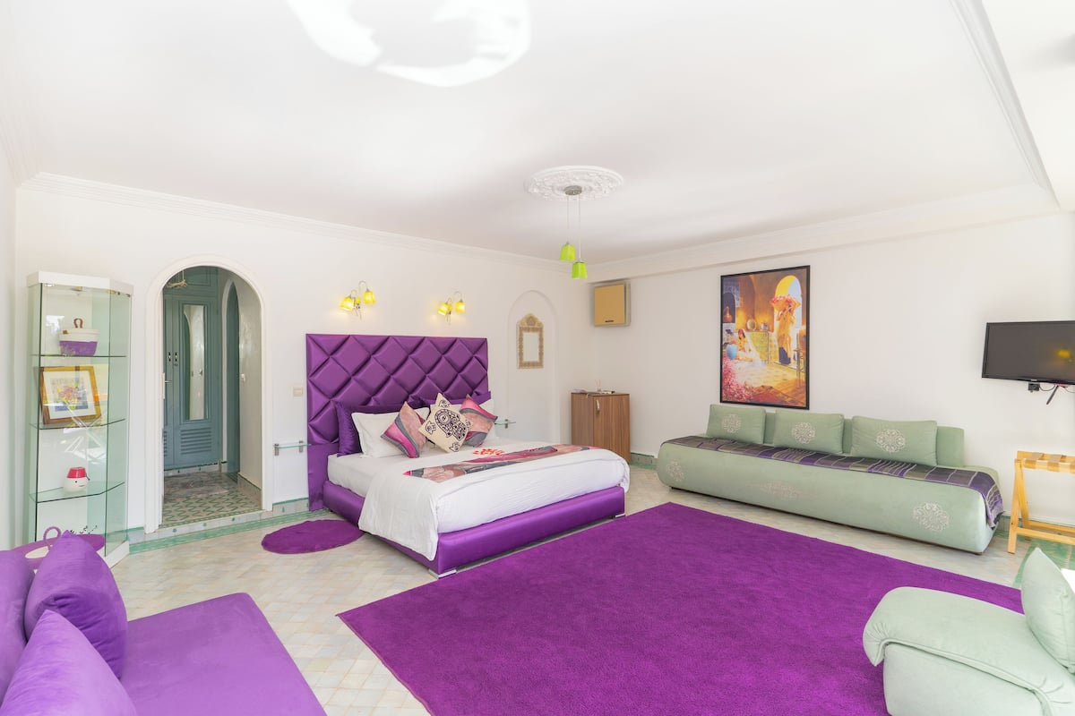 A bedroom with a bed, a sofa, a TV, and a painting on the wall.