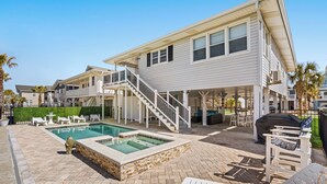 Una casa de dos pisos con piscina, mobiliario exterior y un patio cubierto.