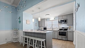Cocina moderna con una isla central, taburetes de bar y un microondas.
