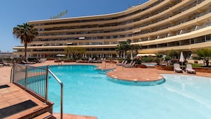 A hotel with a large pool area, multiple balconies, and a clear blue sky.