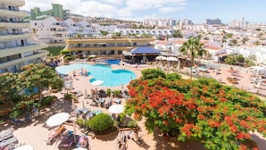 A resort with a central swimming pool, multiple lounge areas, and a variety of buildings in the background.