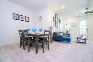 Ein modernes Wohnzimmer mit Essbereich, ausgestattet mit einem blauen Sofa, einem Esstisch mit Stühlen und gerahmten Bildern an den Wänden.