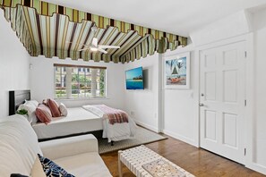 A bedroom with a bed, a sofa, a ceiling fan, a window with blinds, a painting, and a door. - Palm Beacher - Heated Salt Water Pool (Fort Lauderdale)