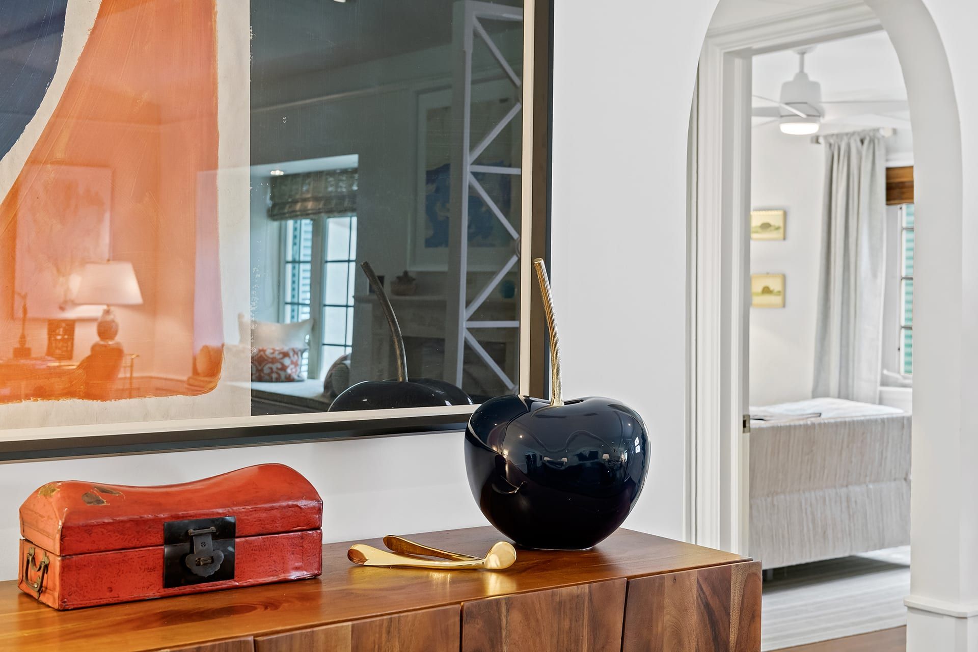A room with a wooden cabinet, a red suitcase, and a black vase on the table.
