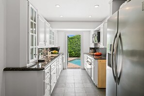 A modern kitchen with white cabinetry, stainless steel appliances, and a view of a swimming pool.