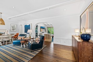 A spacious living room with a dining area, featuring a large mirror, a blue sofa, and a wooden coffee table. - Palm Beacher - Heated Salt Water Pool (Fort Lauderdale)