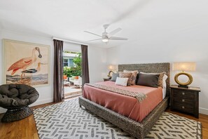 Une chambre à coucher avec un lit, un ventilateur de plafond, une table de chevet et une vue sur l’extérieur.