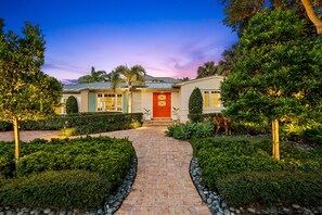 A residential house with a brick pathway leading to the entrance, surrounded by well-maintained hedges and trees. - Palm Beacher - Heated Salt Water Pool (Fort Lauderdale)