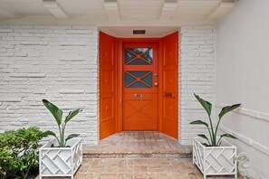 Fachada de ladrillo blanco con una puerta naranja brillante, número 700, y un pequeño escalón que lleva a la entrada.