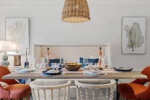 Un comedor con una mesa dispuesta para cuatro, rodeada de sillas, una lámpara colgante y cuadros en las paredes.