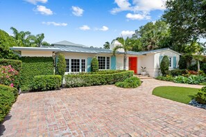 A two-story house with a brick driveway, a red door, and a well-maintained garden.