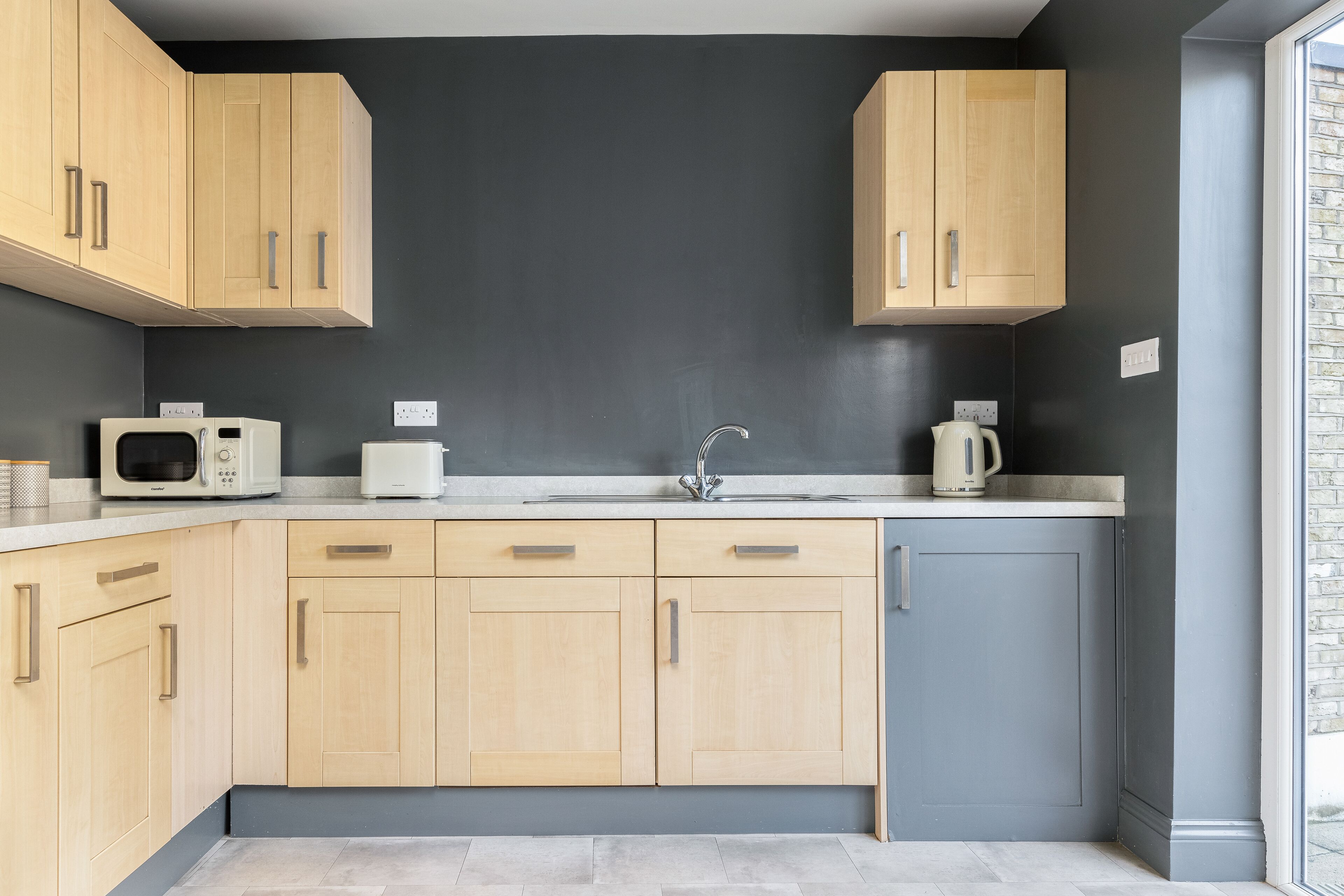 Eine moderne Küche mit hellen Holzschränken, einer dunkelgrauen Spritzschutzwand und einem eingebauten Backofen.