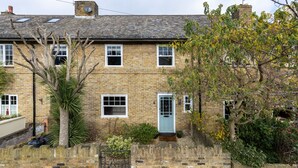 A two-story brick house with a blue door, a small garden, and a tree in front.