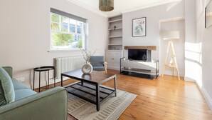 A modern living room with a sofa, coffee table, and TV stand. There is a window with a view of greenery outside.