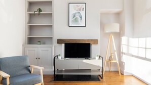 A living room with a television, a blue armchair, a wooden floor, a white cabinet, and a painting on the wall.