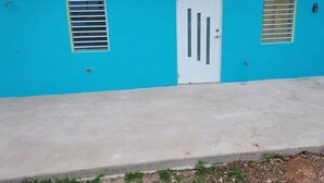 Un edificio con fachada azul, una puerta blanca y dos ventanas con contraventanas.