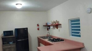 Una cocina compacta con estufa a gas, refrigerador, microondas y una pequeña barra con taburetes.