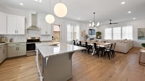 Une cuisine moderne avec des meubles blancs, un grand îlot central et un coin repas comprenant un canapé et des chaises.