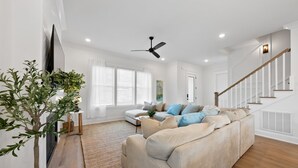 Un salon spacieux avec un canapé d’angle beige, un plancher en bois, un ventilateur de plafond et un escalier avec des rampes blanches.
