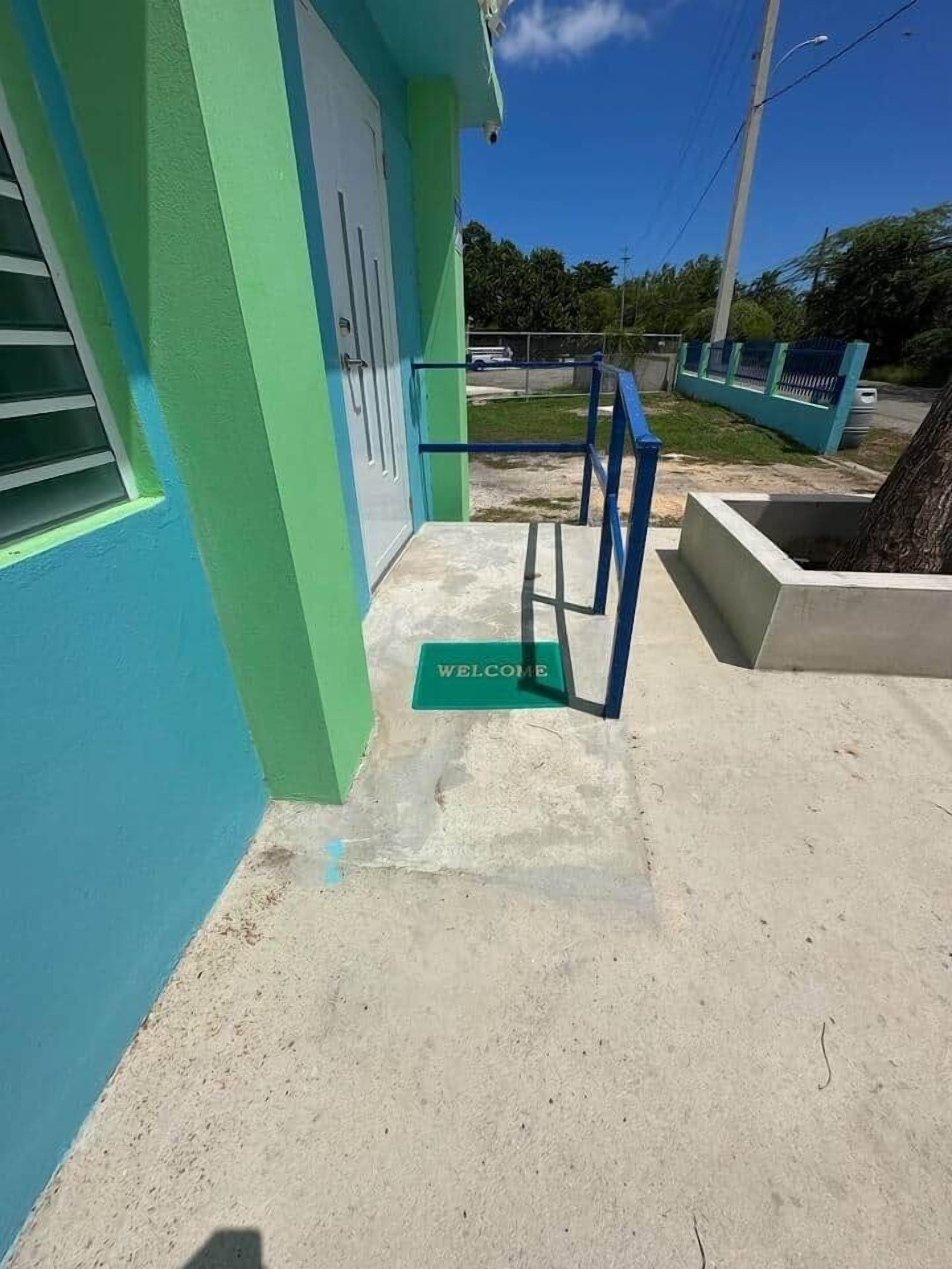 A building with a green and blue exterior, a concrete entrance area, and a metal handrail.