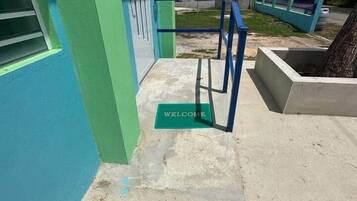 A building with a green and blue exterior, a concrete entrance area, and a metal handrail.