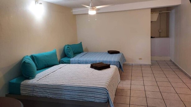 A small, well-lit room with two beds, a ceiling fan, and a visible bathroom door.
