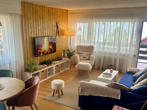 Ein Wohnzimmer mit Fernseher, einem gemütlichen Sessel, einer Couch, einem Couchtisch und einem Essbereich.