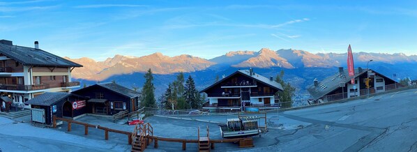 A mountain resort with chalet-style buildings, a ski lift, and a view of snow-capped peaks.