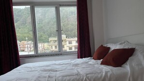A hotel room with a bed, red curtains, and a window with a view of buildings and greenery. - Mount Star Homestay (Kathmandu)