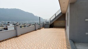 A rooftop terrace with patterned flooring, a staircase leading to an upper level, and a view of a cityscape with mountains in the background. - Mount Star Homestay (Kathmandu)