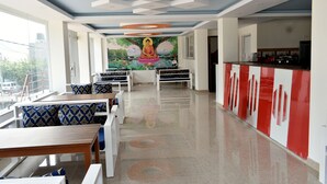 A modern hotel lobby with a mural of a meditating figure, seating areas, and a kitchen counter. - Mount Star Homestay (Kathmandu)