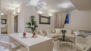 En moderne stue med en hvid sofa, et glasbord og en stor dekorativ ventilator. Der er en potteplante og en vase med blomster på bordet.