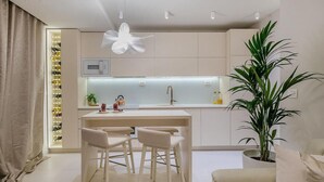 Et moderne køkken med en central ø, to barstole, en stor potteplante og et vinskab.