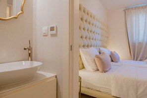 A bedroom with a large, tufted headboard, a round sink, and a bedside table. - Levelup Apartment Split (Split)
