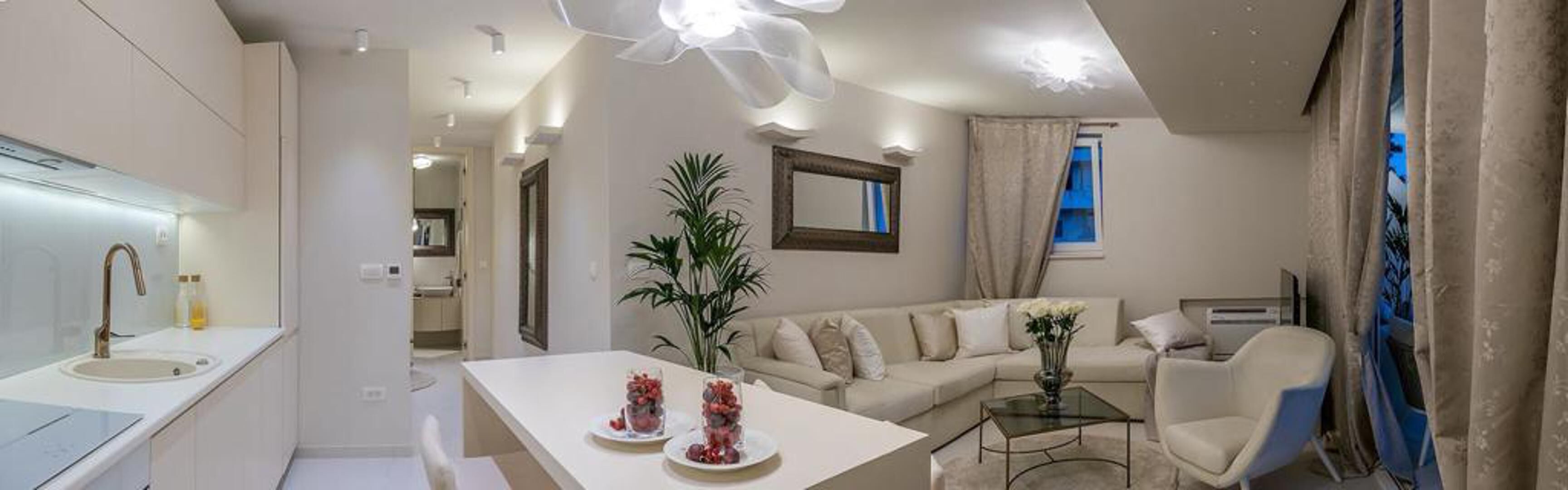 Un salon moderne avec un canapé, une table basse et un coin repas comprenant une table blanche et deux assiettes de fruits.