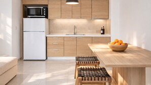 Une cuisine moderne avec des meubles en bois, un réfrigérateur blanc, un four à micro-ondes, un évier et une table en bois sur laquelle se trouve un saladier rempli d’oranges.