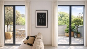 Un salon moderne avec un canapé, une œuvre d’art encadrée et une vue sur un balcon agrémenté de plantes en pot.