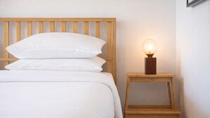 Un lit avec une literie blanche, une tête de lit en bois et une table de chevet avec une lampe.