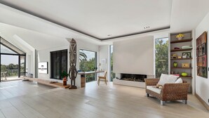 A spacious living room with a fireplace, a dining area, and a large window offering a view of palm trees.