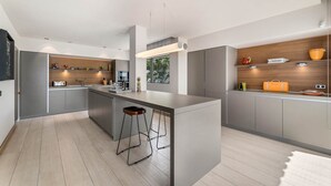A modern kitchen with a central island, bar stools, and a view of a garden through a window.
